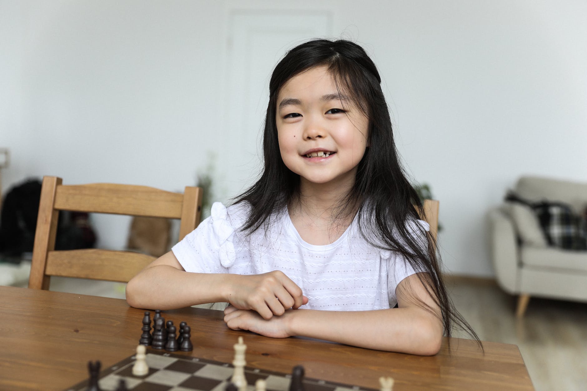 happy cute asian girl sitting at table with chessboard