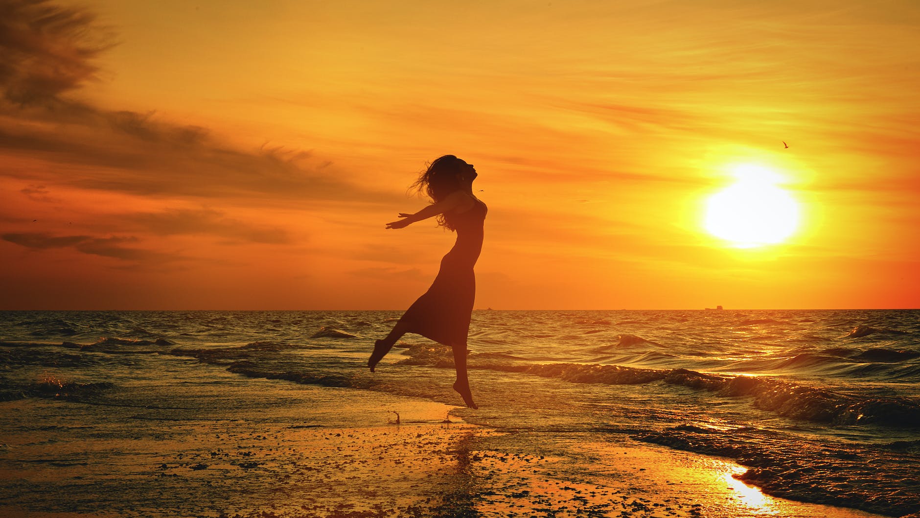 silhouette of unrecognizable woman jumping above sea beach at sunset