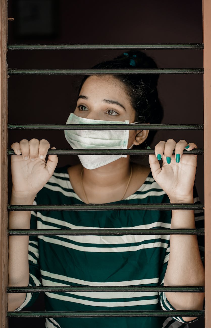 woman in green and white stripe shirt covering her face with white mask