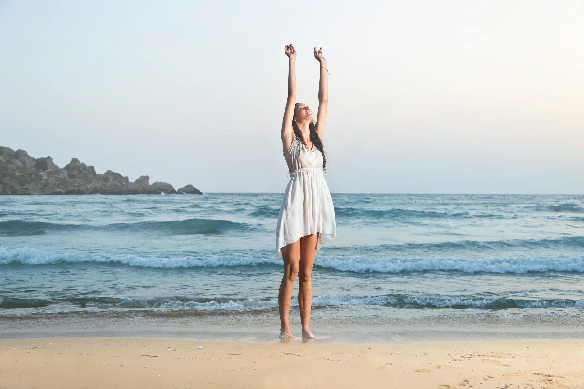 photo of woman in white sleeveless dress raising hands
