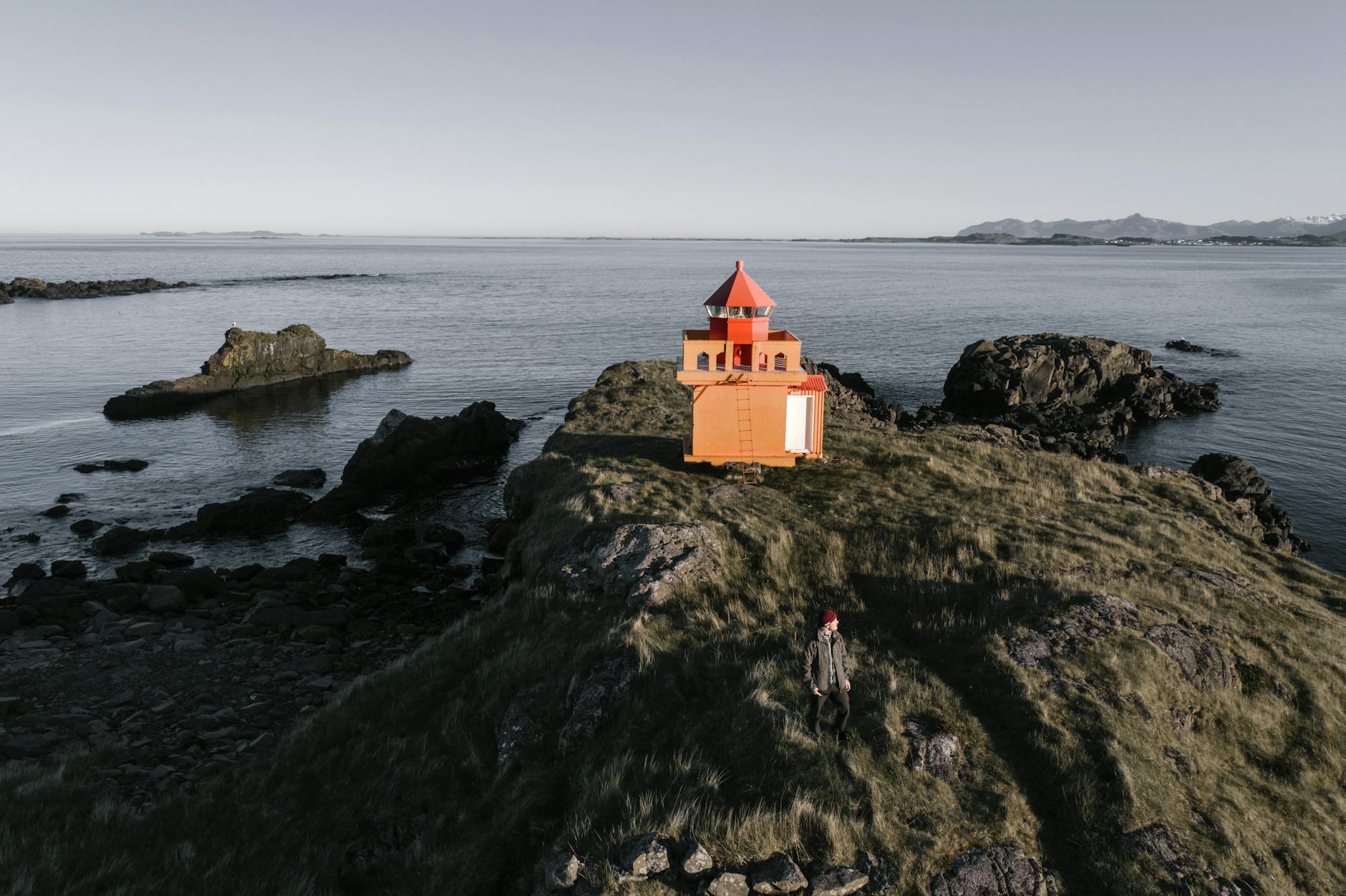 lightkeeper near orange lighthouse on rough rocky shore