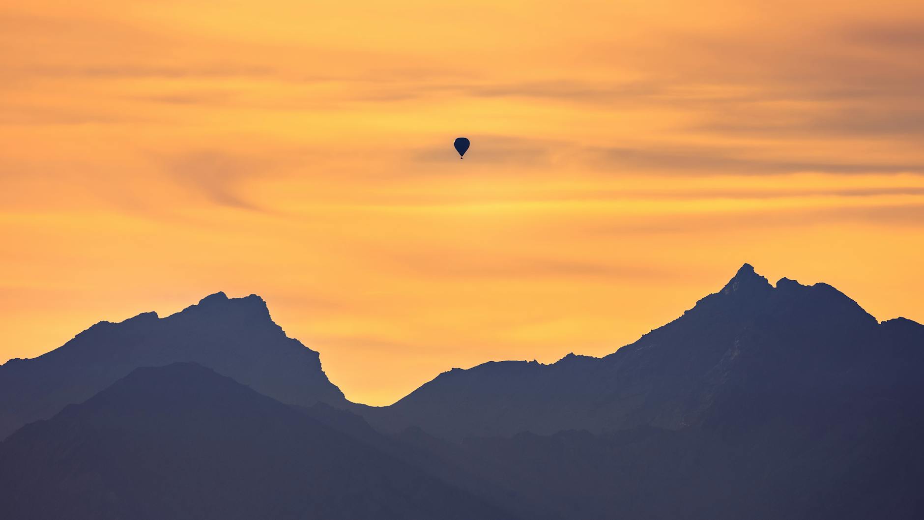 hot air balloon flying over the mountains during sunset