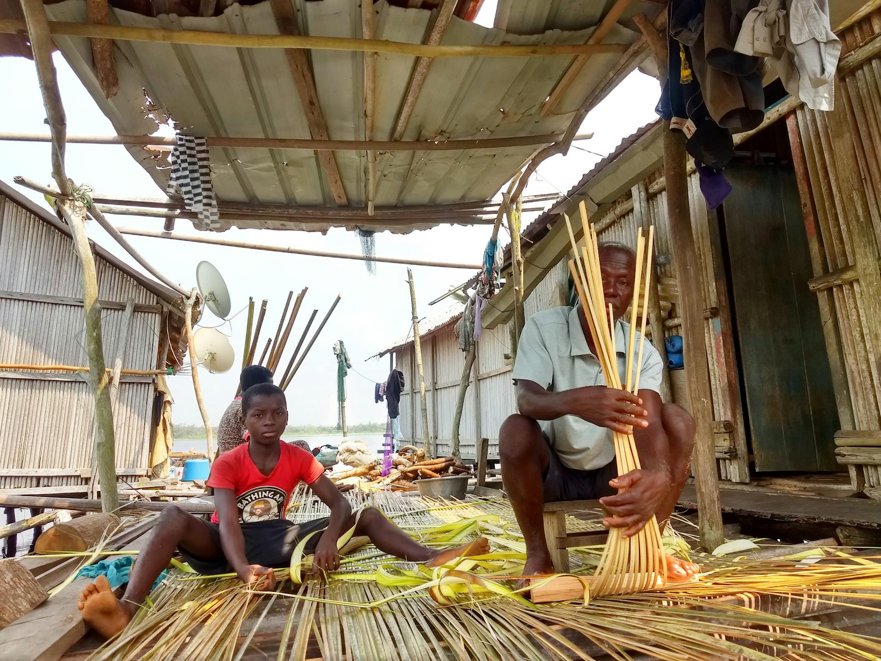 people weaving bamboo outside their wooden house