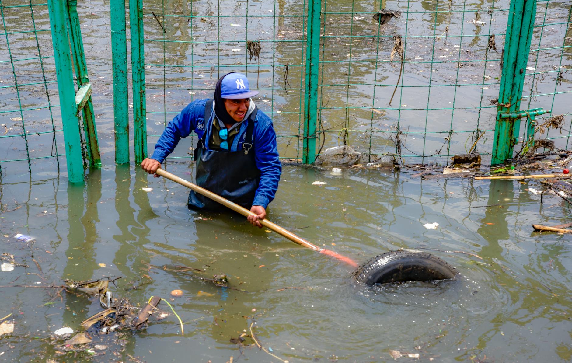 worker clearing debris from polluted floodwater