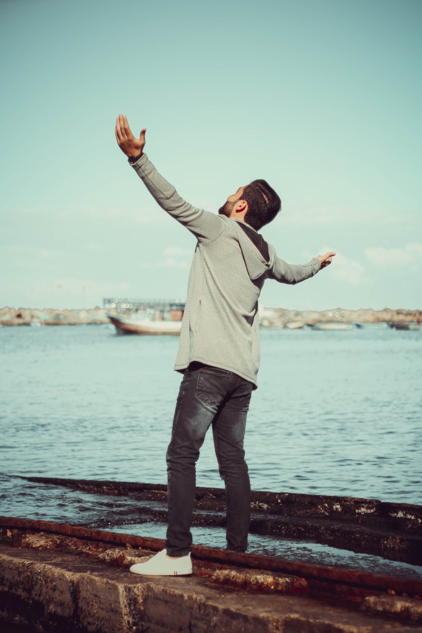 man in grey hoodie standing on grey pavement near sea